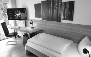 Modernes Hotelzimmer in Schwarz-Weiß mit Schreibtisch, Fernseher und gemütlichem Bett im Haus Stallmeister, Lippstadt