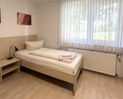 Einzelzimmer für Handwerker im Haus Stallmeister in Lippstadt mit modernem Bett, Kleiderschrank und großem Fenster.
